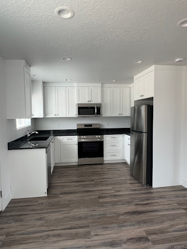 Modern kitchen in Priority Homes Apartments, featuring white cabinetry, stainless steel appliances, and black countertops, designed for functional living in Nephi, Utah.